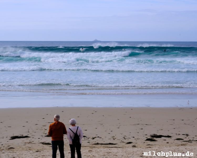 Zwei Touristen schauen Surfern in der Baie des Trespasses zu.
