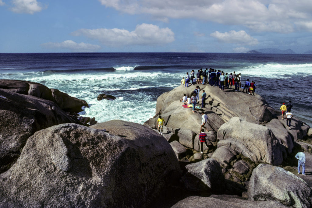 Die besten Surf-Inseln der Welt: Brasilien, Santa Catarina, Zuschauer auf Granitblöcken am Strand von Joaquina