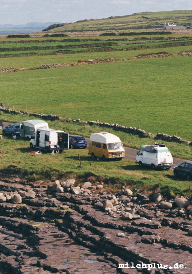 Mehrere Campingbusse stehen an einer Küstenstraße in Irland