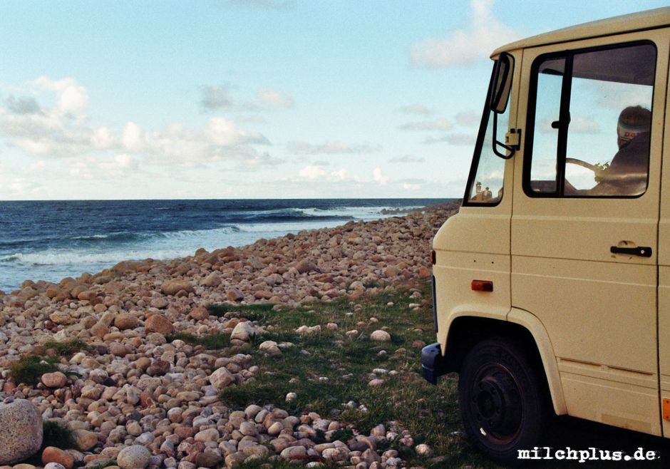 Ein Düdo steht mit Blick aufs Meer auf einem Steinstrand